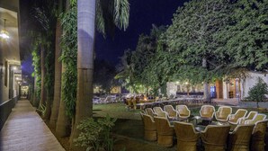 An outdoor seating area with wicker chairs and tables, surrounded by greenery and trees. - Hotel Ranthambore Regency (Sawai Madhopur)