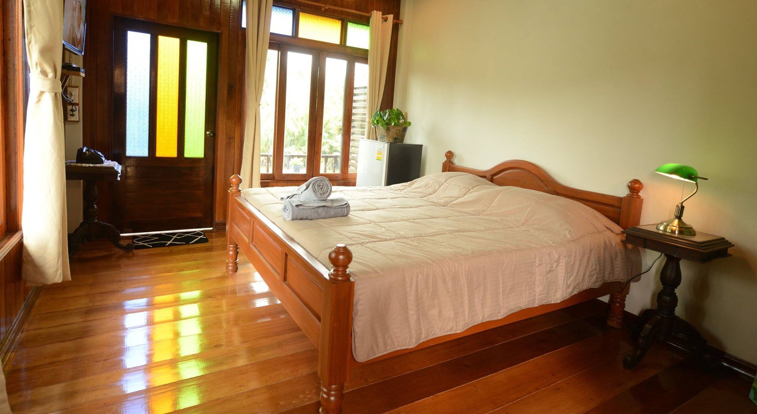 A wooden bed with a white bedspread, a bedside lamp, and a potted plant on a nightstand.
