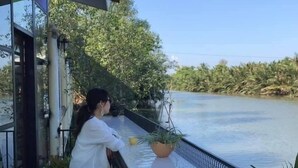 A person sitting on a balcony with a view of a river and greenery. - River Jam Amphawa (Amphawa)