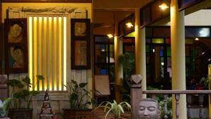 A warmly lit interior with vertical blinds, framed artwork, and potted plants. - River Jam Amphawa (Amphawa)