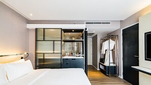 Ein modernes Hotelzimmer mit einem großen Bett, einem Badezimmer mit Glasdusche, einem begehbaren Kleiderschrank und einem an der Wand montierten Fernseher.
