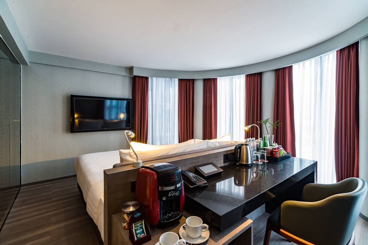 Een hotelkamer met een bed, een bureau met koffiezetapparaat, een televisie en een raam met gordijnen.
