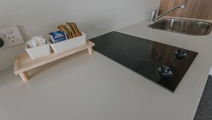 Una cucina moderna con piano cottura a induzione nero, lavello in acciaio inossidabile ed un ripiano in legno con gli utensili da cucina.
