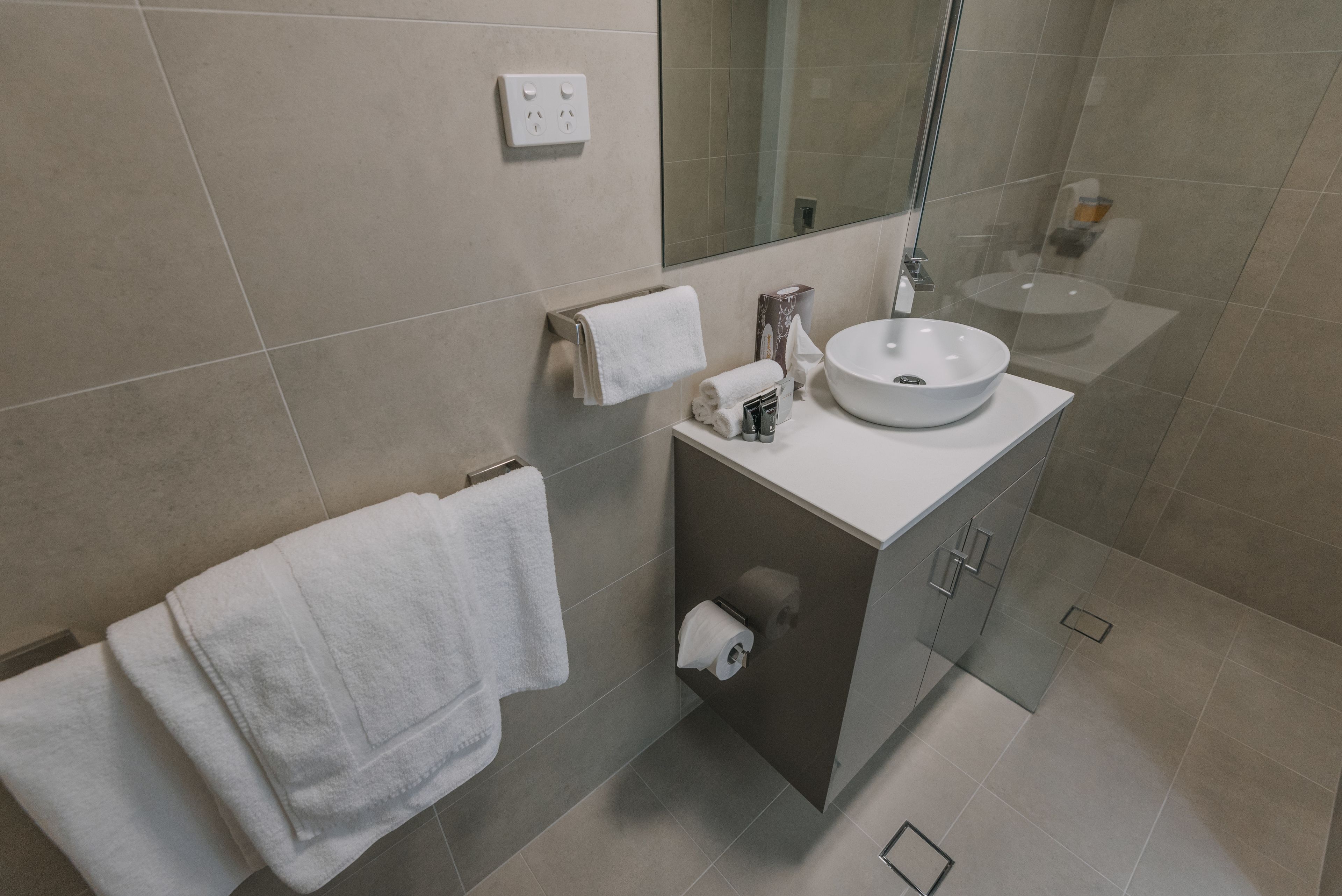 Une salle de bain moderne avec un lavabo blanc, un porte-serviettes, un distributeur de papier toilette et un miroir.