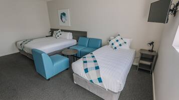 A hotel room with two beds, a sofa, a small round table, and a TV mounted on the wall.