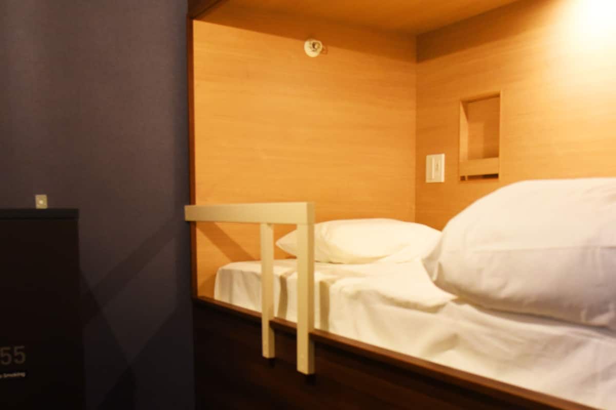 Ein kleines Hotelzimmer mit einem Einzelbett, einem Tisch und einem hölzernen Kopfteil.