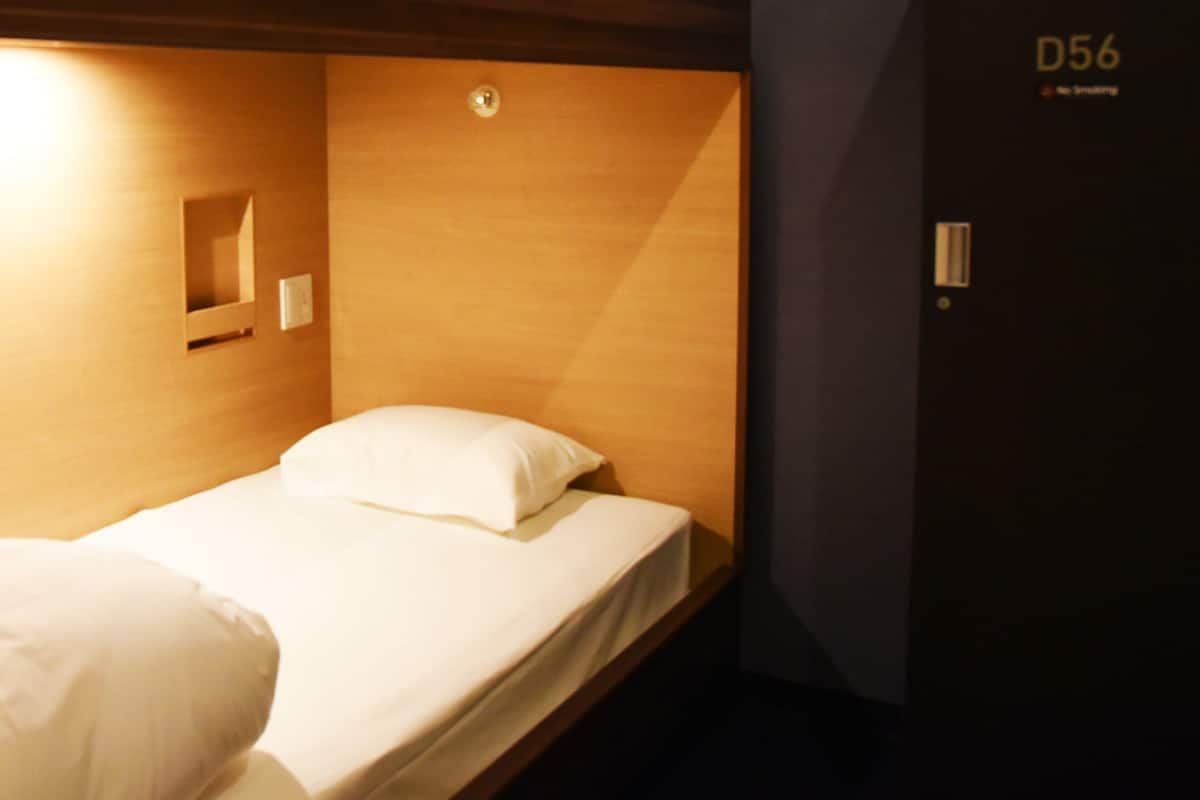 Ein Einzelbett mit Holz-Kopfteil, einer kleinen Ablage und einer Tür mit der Aufschrift 'D56'.