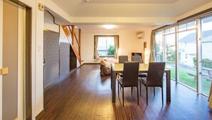 A spacious dining area with a wooden floor, a large window, and a view of the outdoors. - Kitakara Yuimaru in Motobu (Motobu)