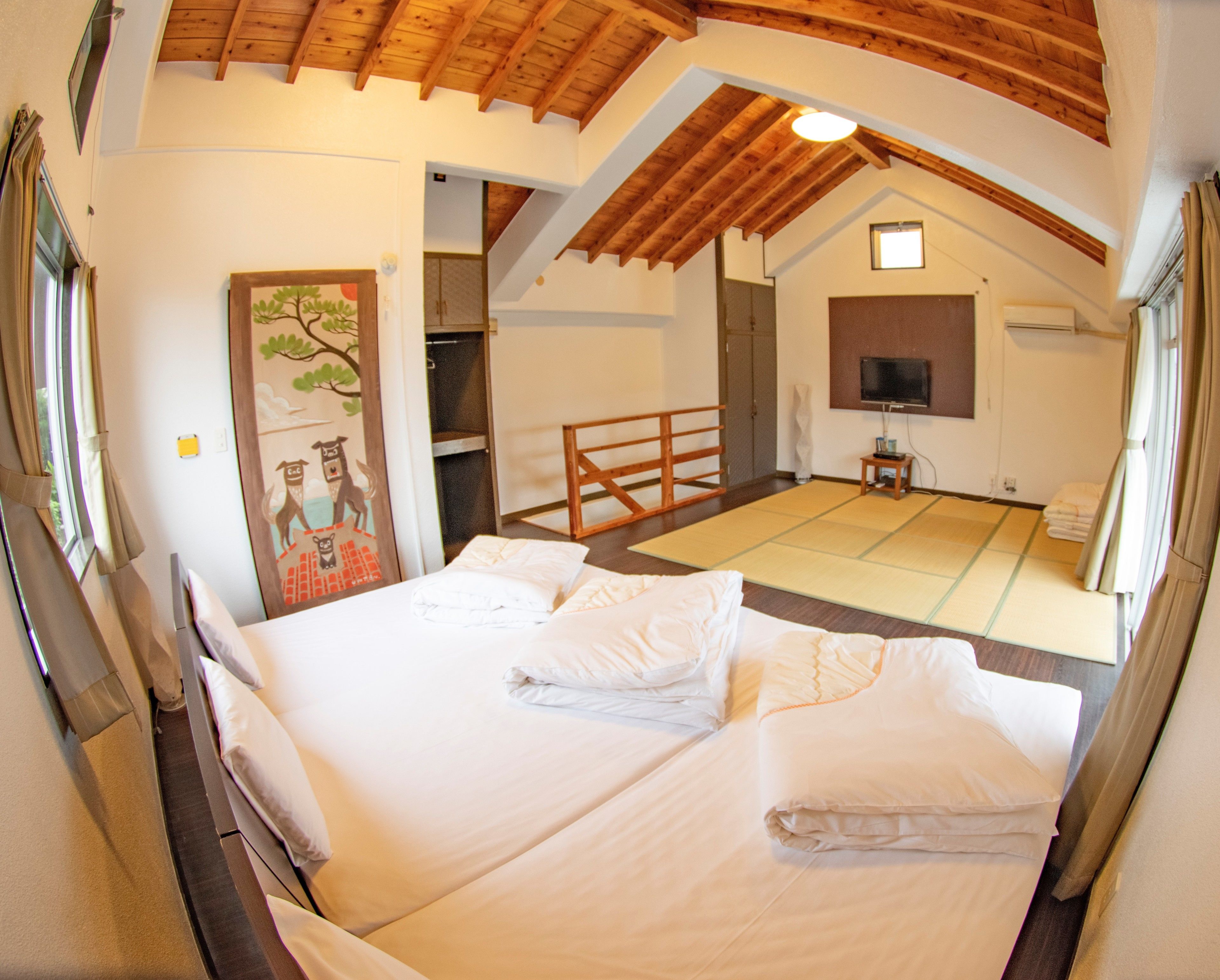 A room with a large bed, a tatami mat, a wooden ceiling, and a television.