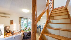 A modern living room with a wooden staircase, a sofa, and a dining area. - Kitakara Yuimaru in Motobu (Motobu)
