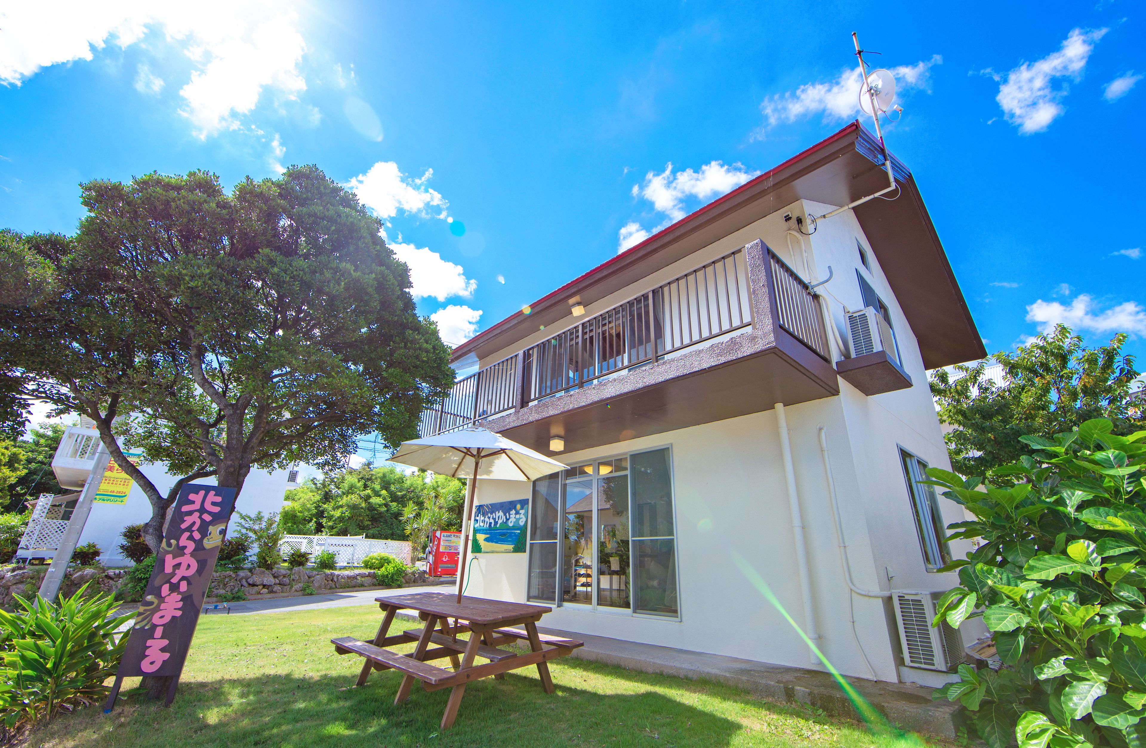 A two-story building with a balcony, a picnic table, and a sign in a foreign language.