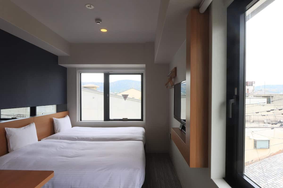 Une chambre d’hôtel avec deux lits, une télévision et une grande fenêtre donnant sur la ville.