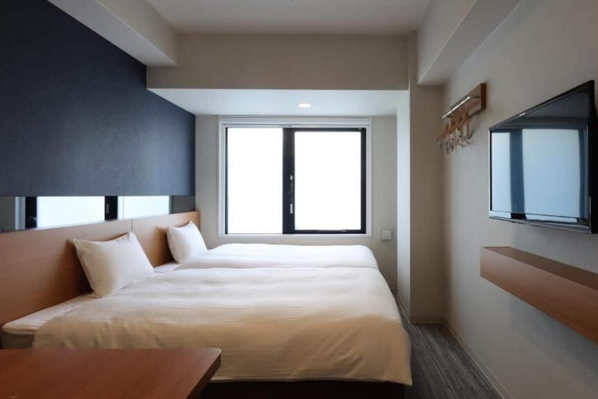 Une chambre d’hôtel dotée d’un grand lit, d’un téléviseur fixé au mur et d’une fenêtre laissant entrer la lumière naturelle.