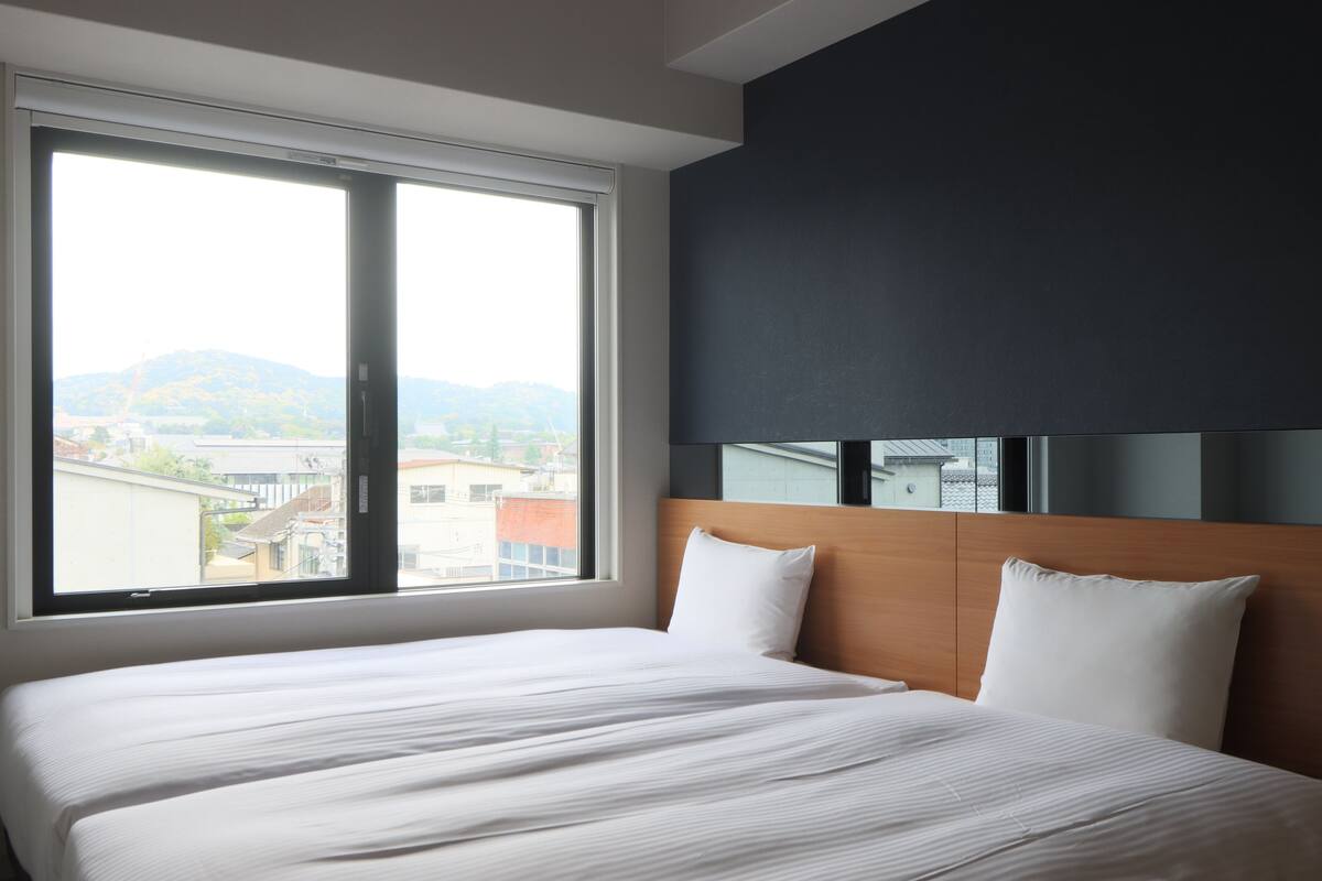 Une chambre d’hôtel avec un grand lit, un mur de couleur sombre et une fenêtre donnant sur la ville.