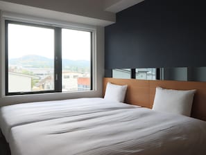 A hotel room with a large bed, a dark wall, and a window with a city view.