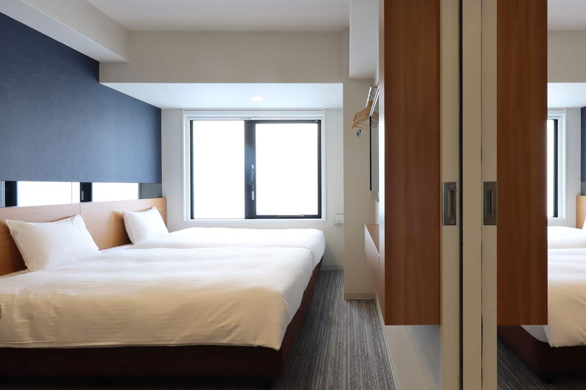 Une chambre d’hôtel avec deux lits, une grande fenêtre et une armoire avec un miroir.