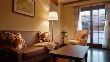 A cozy living room with a brown leather sofa, a wooden coffee table, and a view of mountains through a large window.
