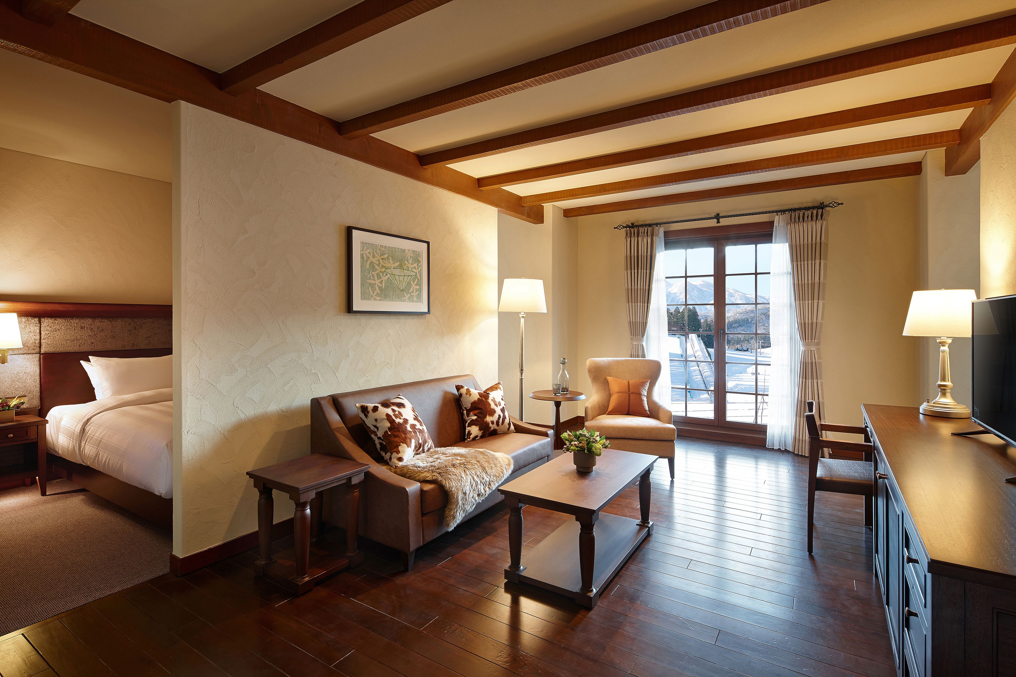 A hotel room with a bed, a sofa, a coffee table, a TV, and a window with curtains.