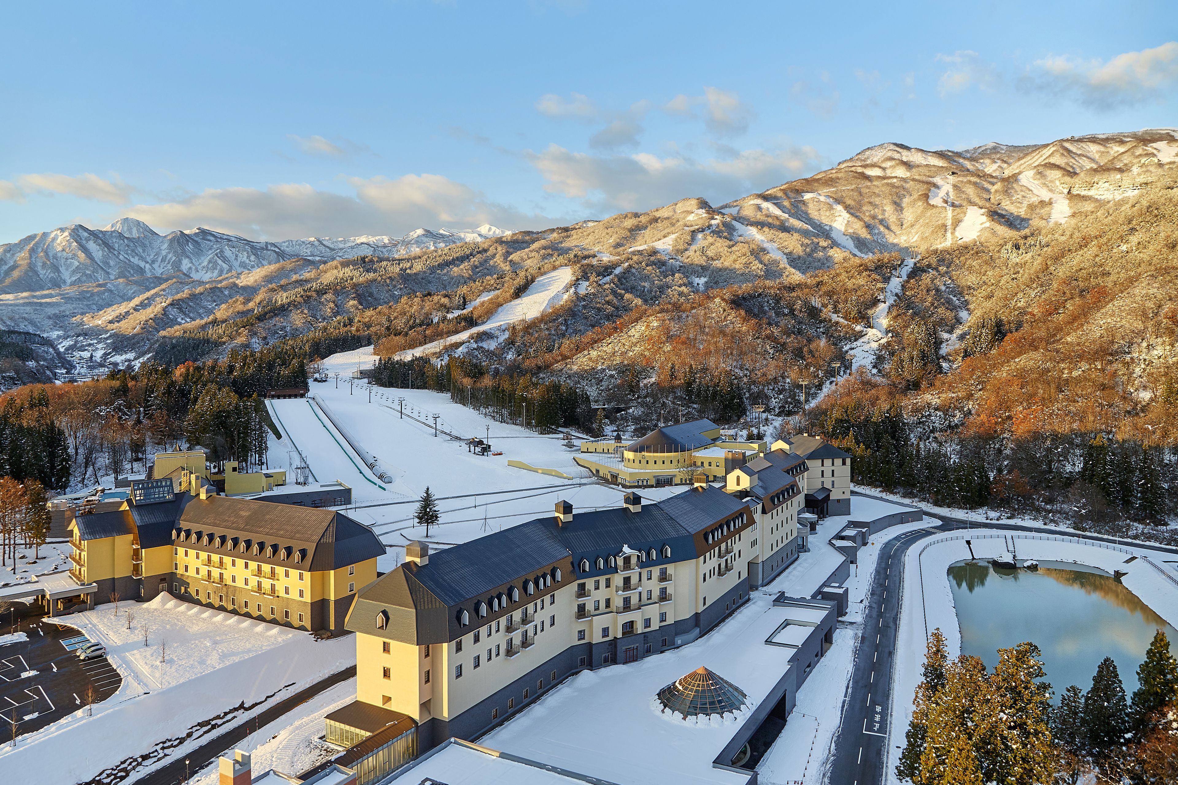 A large hotel with multiple buildings, a ski slope, and a lake.