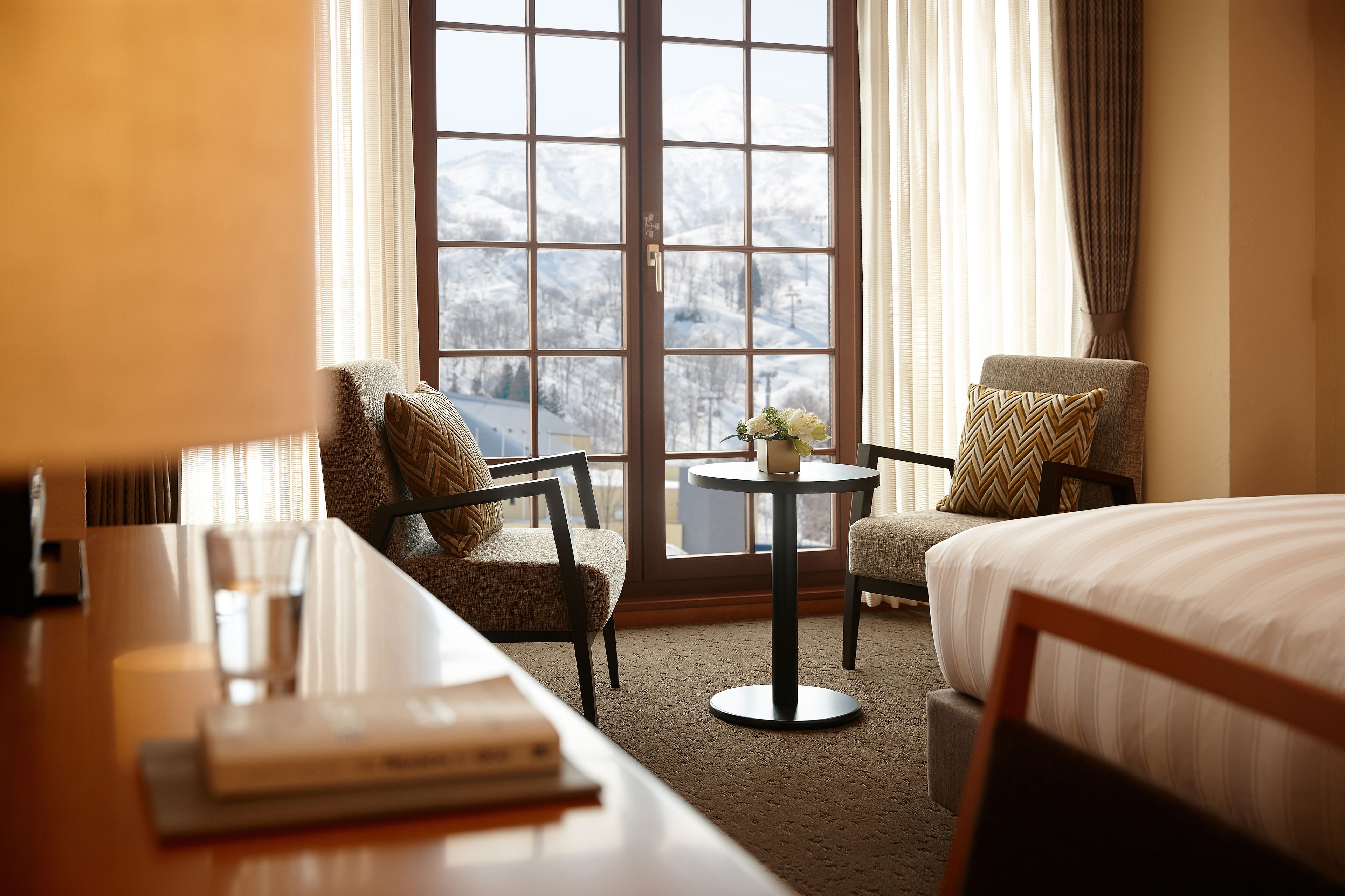 A hotel room with a large window, two chairs, a small table, and a bed.