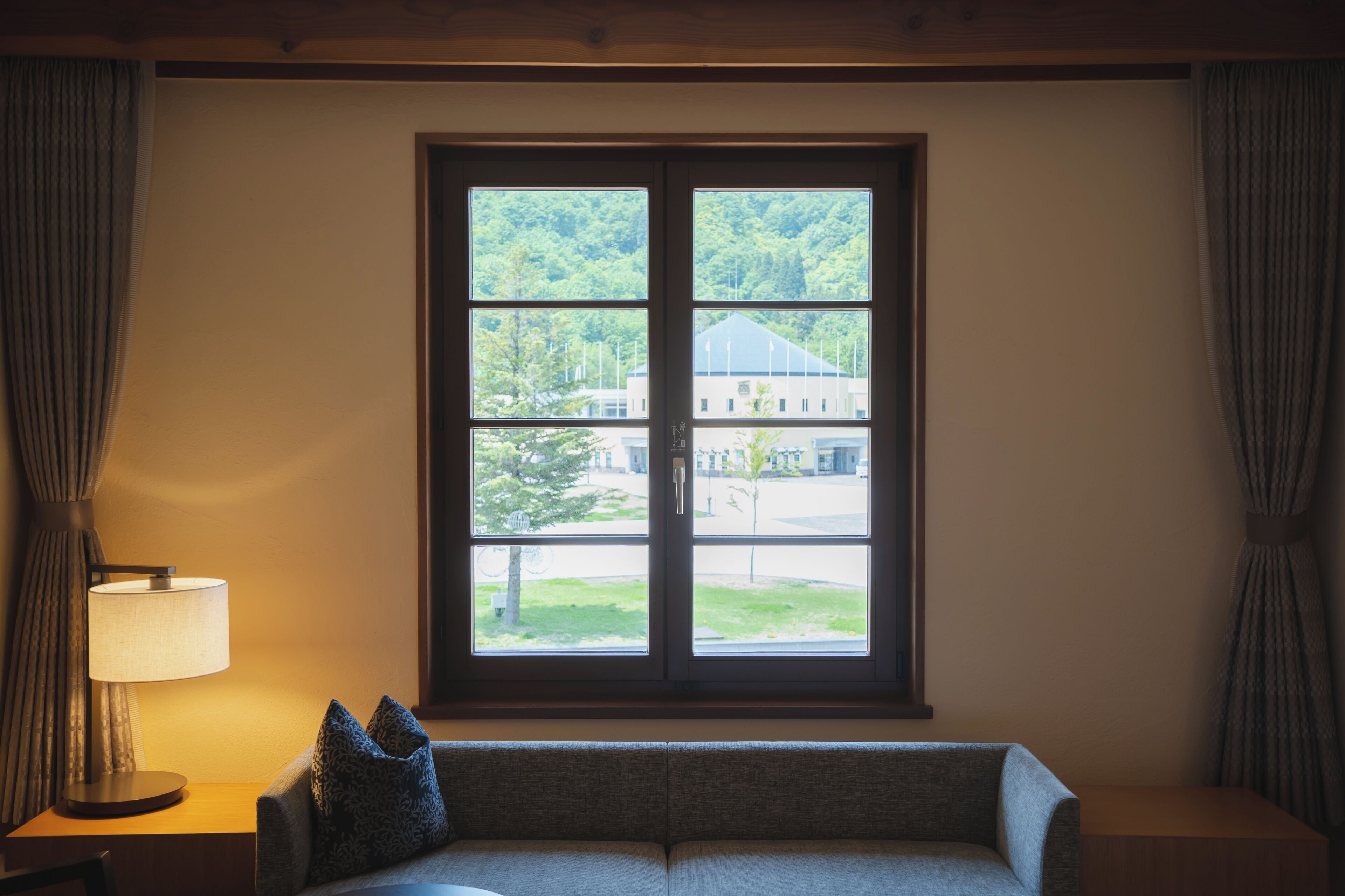 A room with a large window, a sofa, and a lamp.