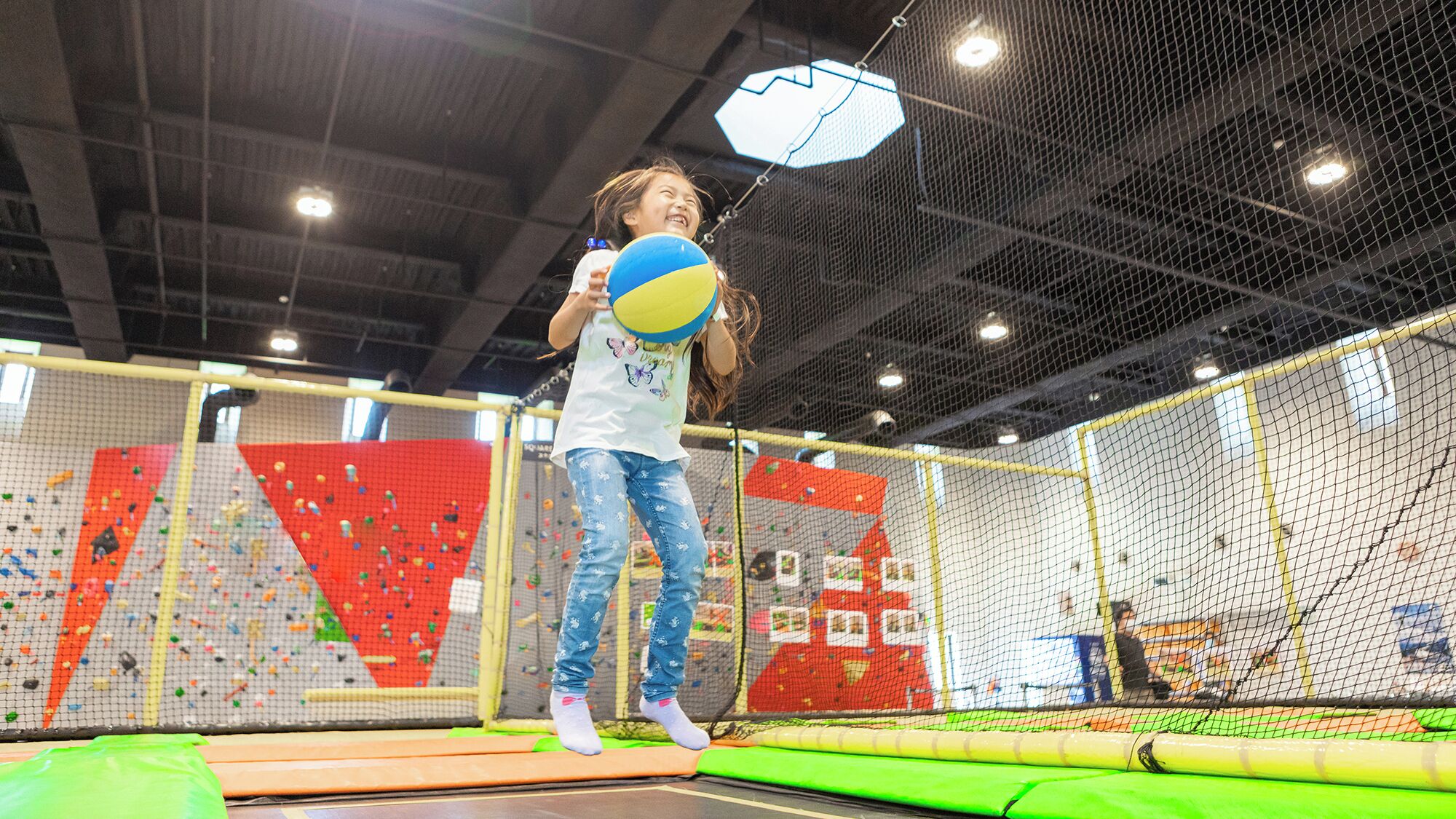 A child playing on a trampoline in an indoor play area with climbing walls and safety nets.