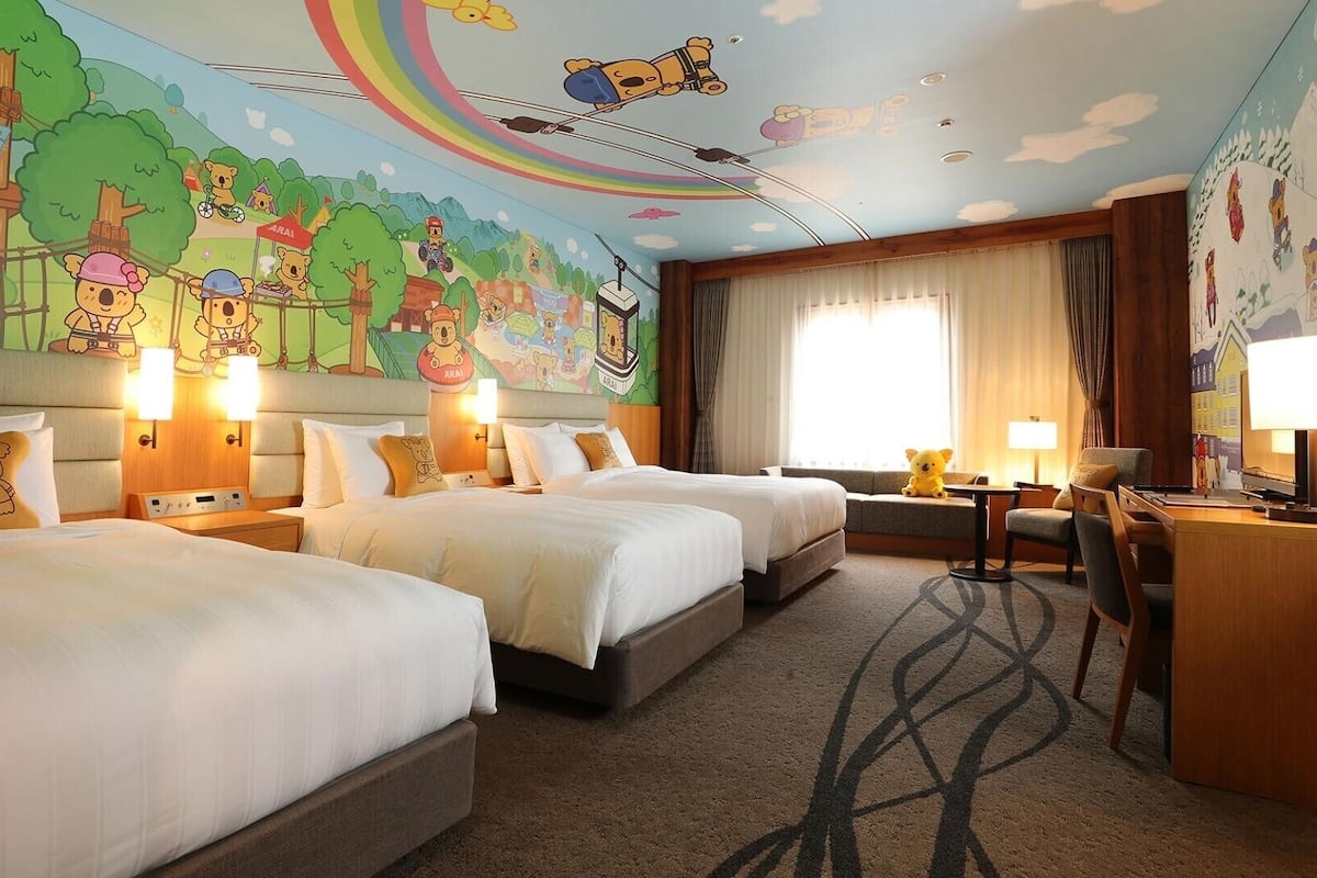 A hotel room with two beds, a desk, and a large mural on the ceiling.