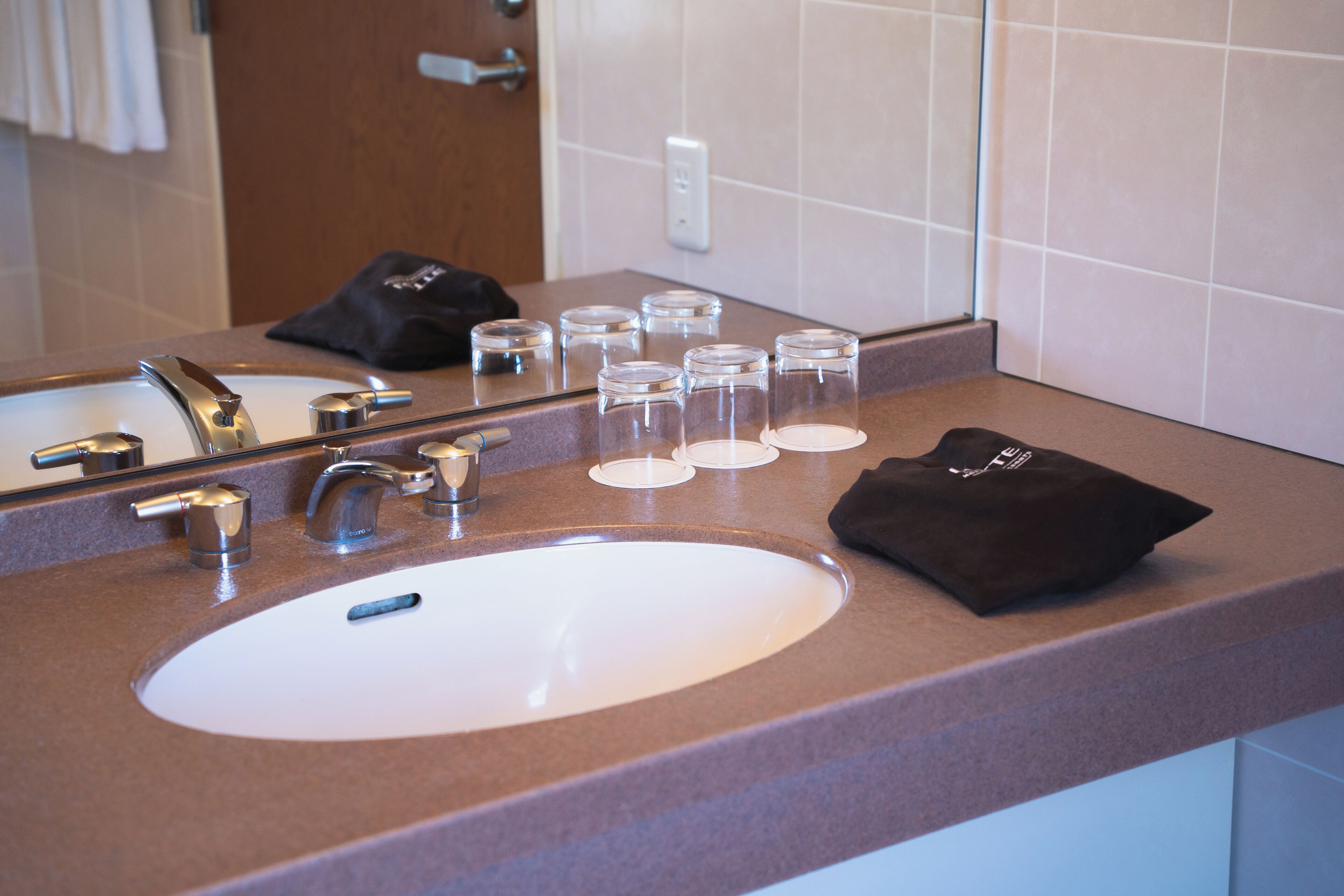 A bathroom sink with a mirror, a towel, and several clear glasses on the countertop.