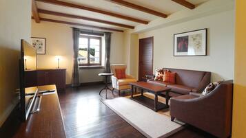 A living room with a wooden floor, a sofa, a coffee table, a TV, and a window with curtains.