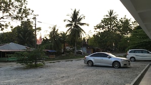 A gravel driveway with parked cars and a small building with a red roof. - Lyaa Resthouse (Langkawi)