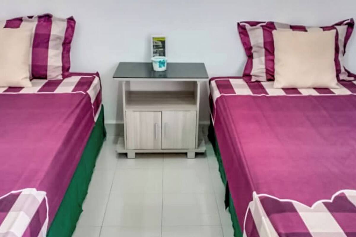 A room with two beds, each with a striped bedspread and matching pillows. There is a small table with a magazine and a cup between the beds.