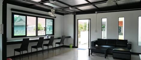 A spacious room with a black ceiling, large windows, a black sofa, and a row of chairs.
