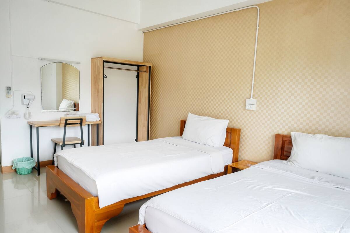 A hotel room with two beds, a desk with a chair, a mirror, and a wall-mounted phone.