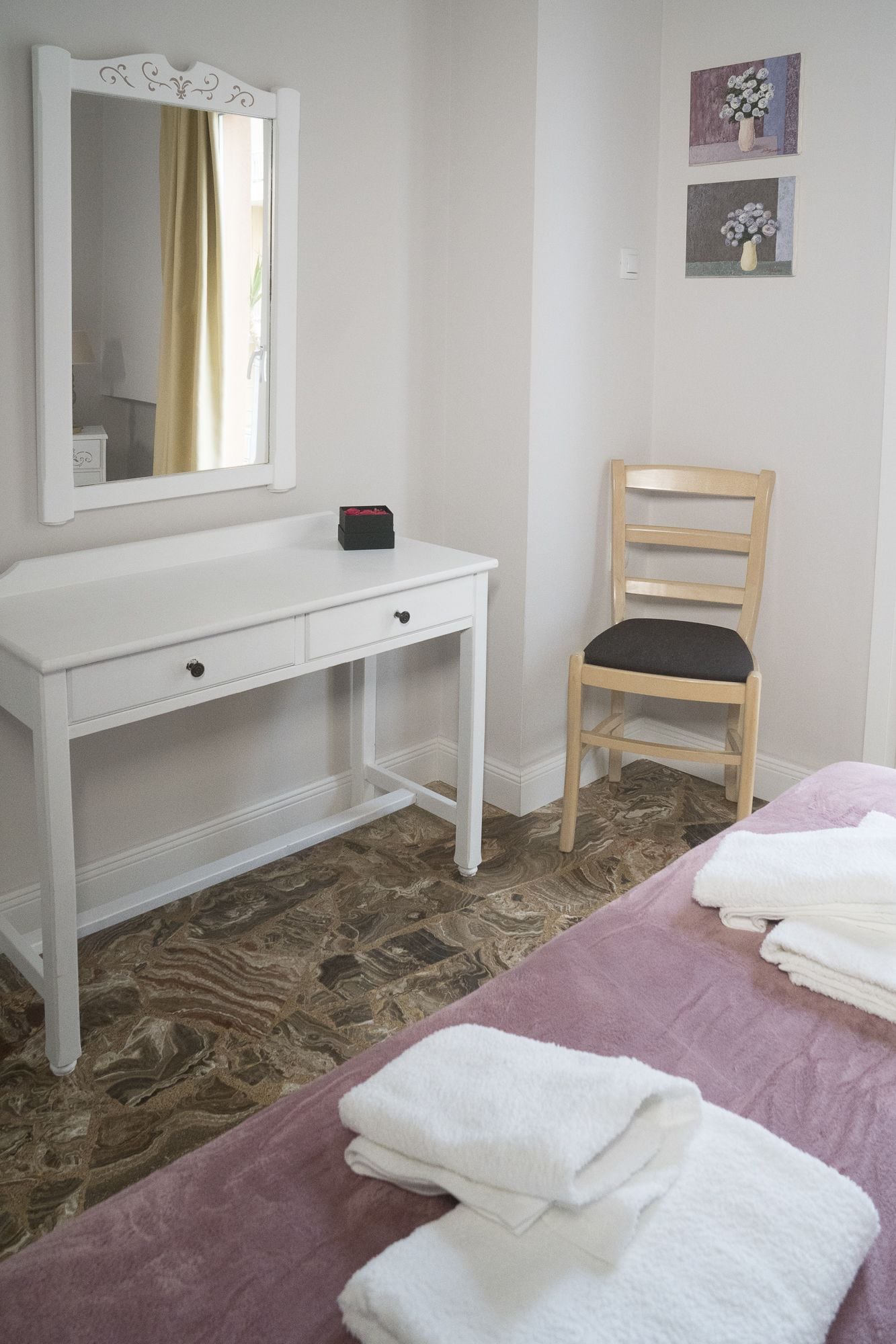 A bedroom with a white dresser, a chair, and a bed with towels.