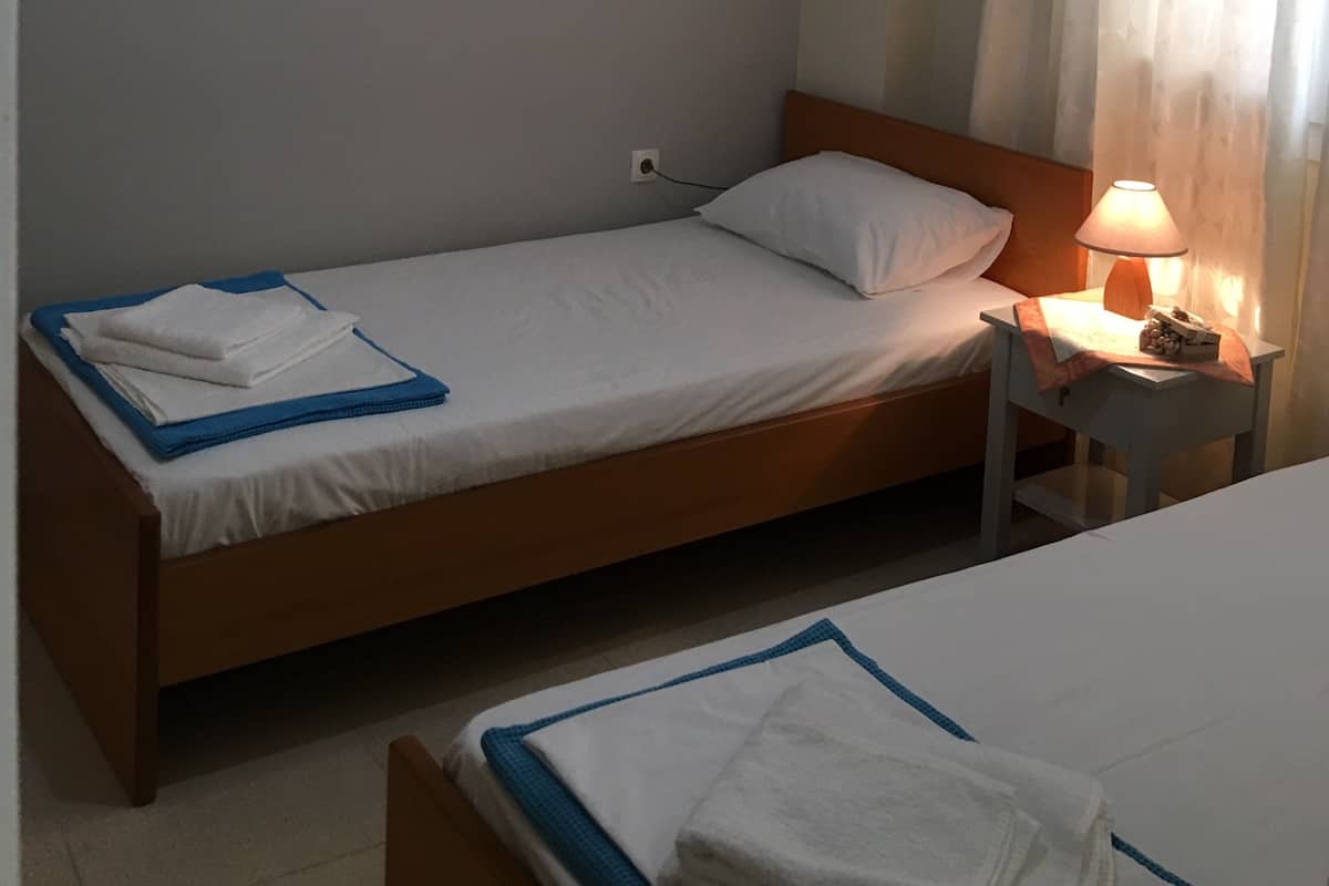 A single bed with a wooden headboard, a bedside table with a lamp, and an air conditioning unit mounted on the wall.