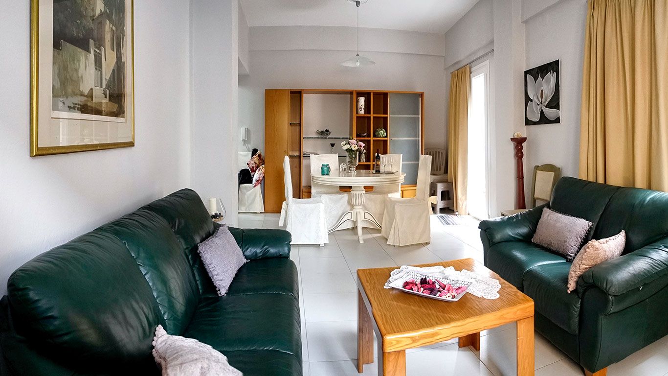 Un salon avec deux canapés en cuir vert, une table basse en bois et, au fond, un coin repas.