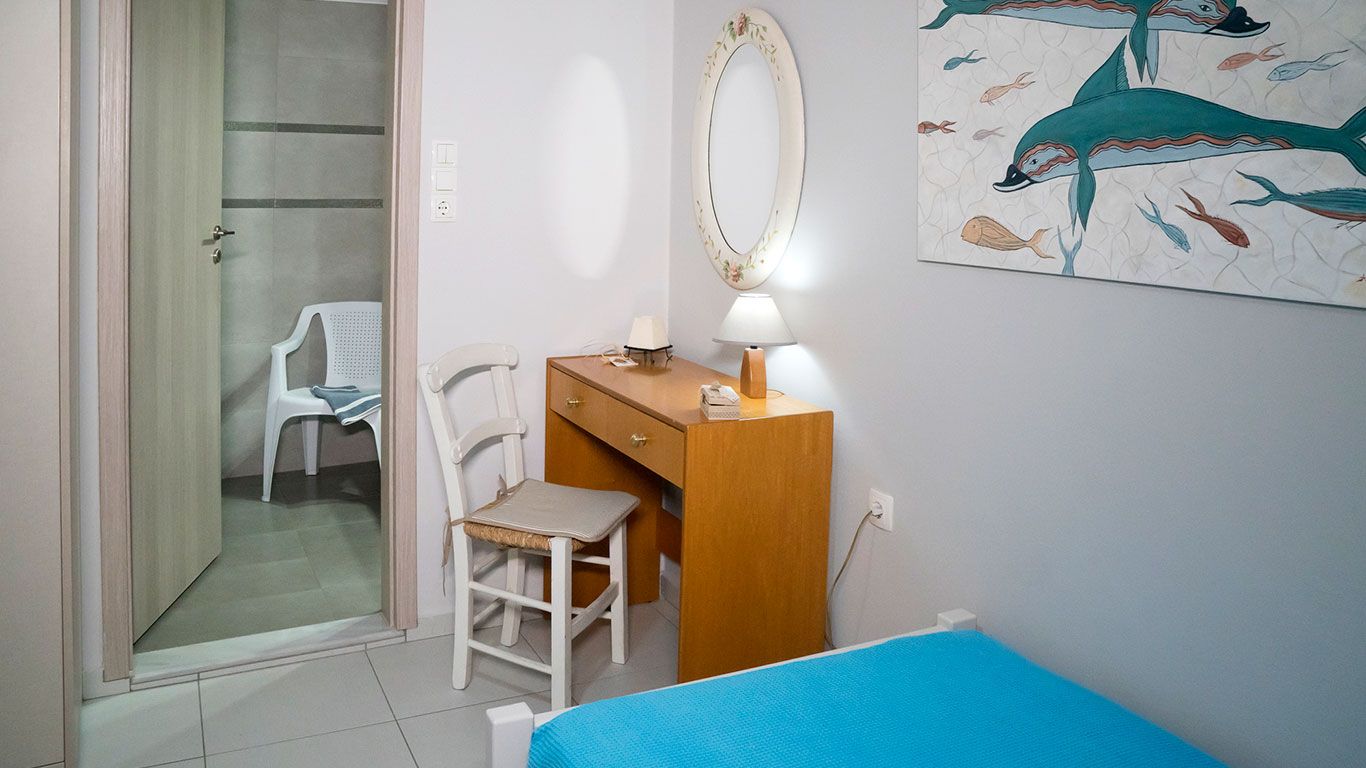 Quarto com cama, escrivaninha com cadeira, espelho e um quadro de peixe na parede.
