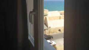 A view through an open window with a view of the sea and buildings in the distance. - Heraklion Old Port Apartments (Heraklion)