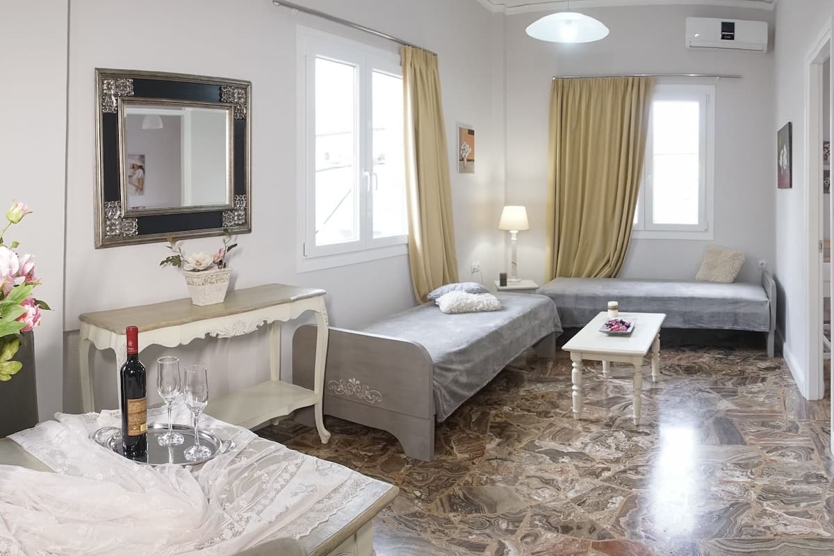 A small, well-lit room with a bed, a sofa, a table, and a mirror.