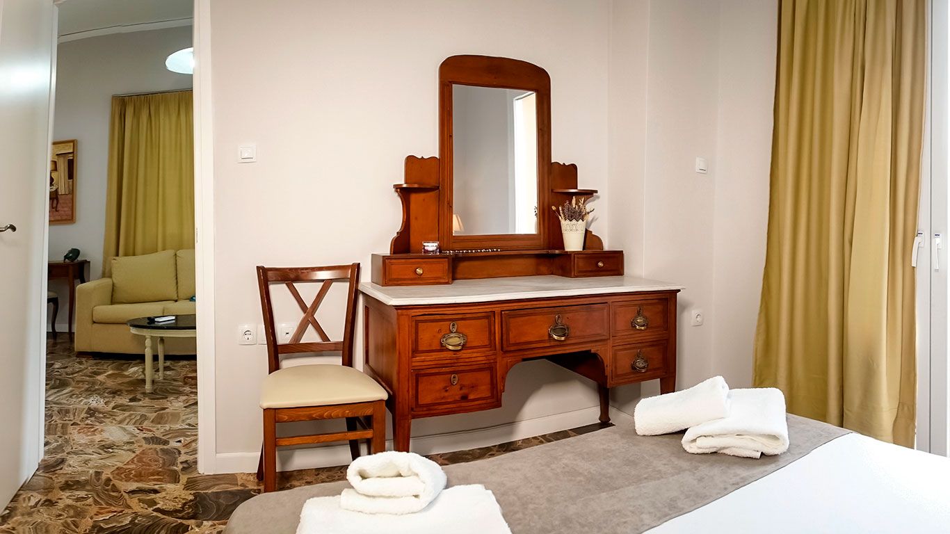 A hotel room with a wooden dresser, a mirror, a chair, a bed, and a pair of towels.
