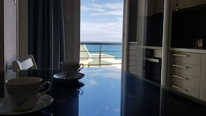 A room with a view of the sea, a table with two cups, and a cabinet.