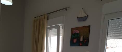 A room with a bed, a small table with chairs, a window with blinds, and a painting on the wall.