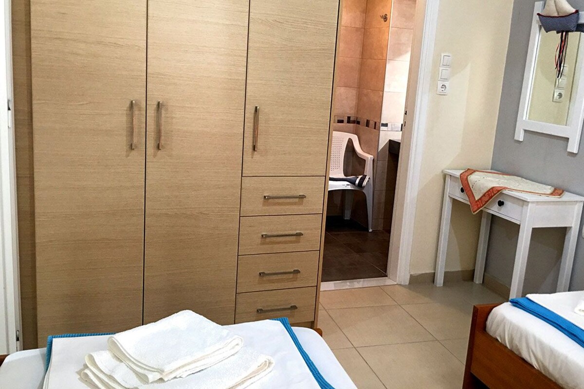 A hotel room with a wardrobe, a desk, and two beds.
