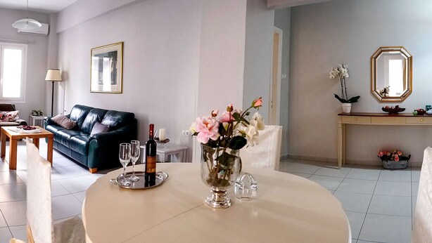 Una sala de estar con un sofá, una mesa de comedor con un florero, una botella de vino y copas.
