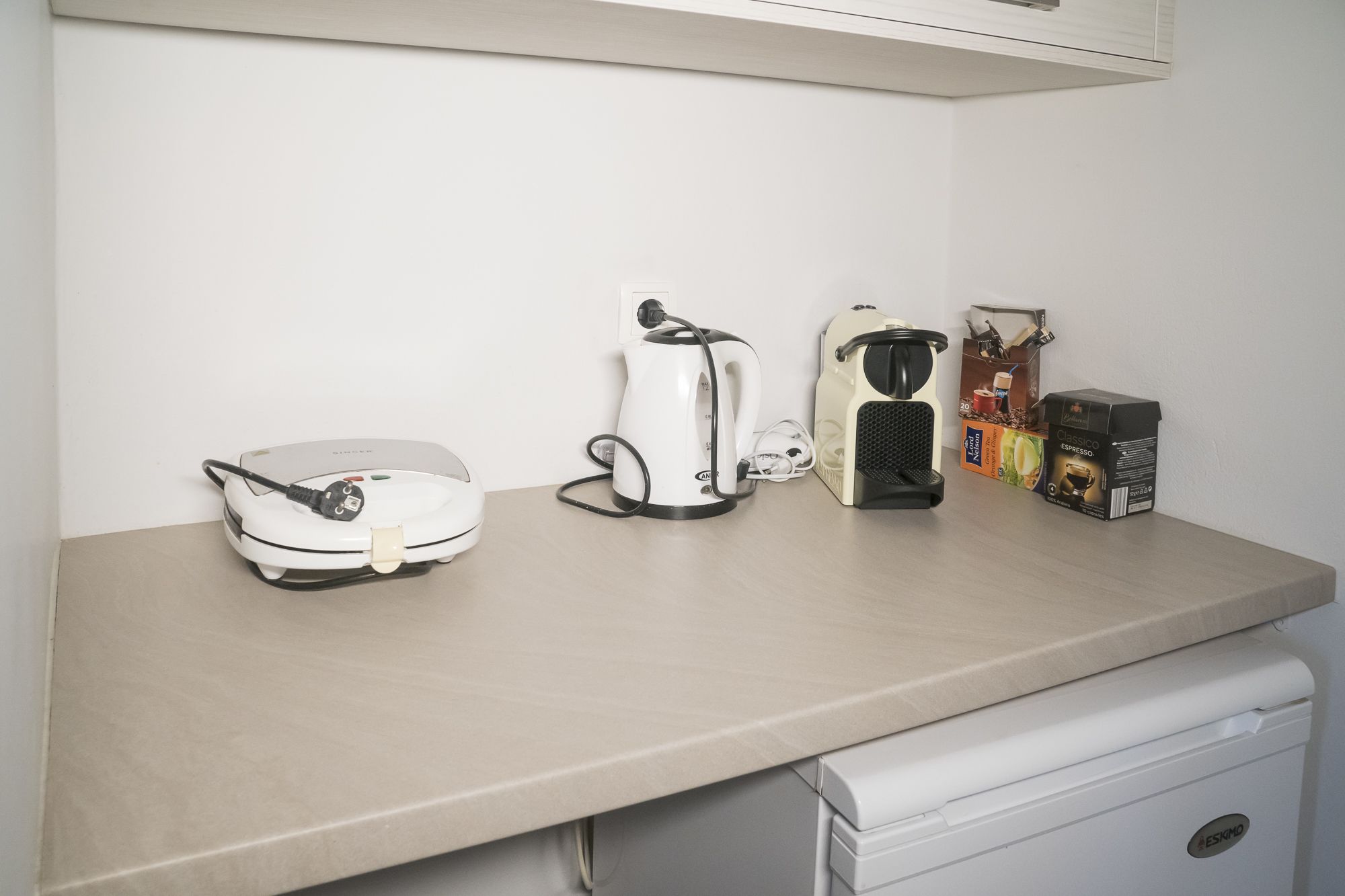 Un piano di lavoro in cucina con una macchina da caffè, un bollitore e una confezione di cialde per il caffè.