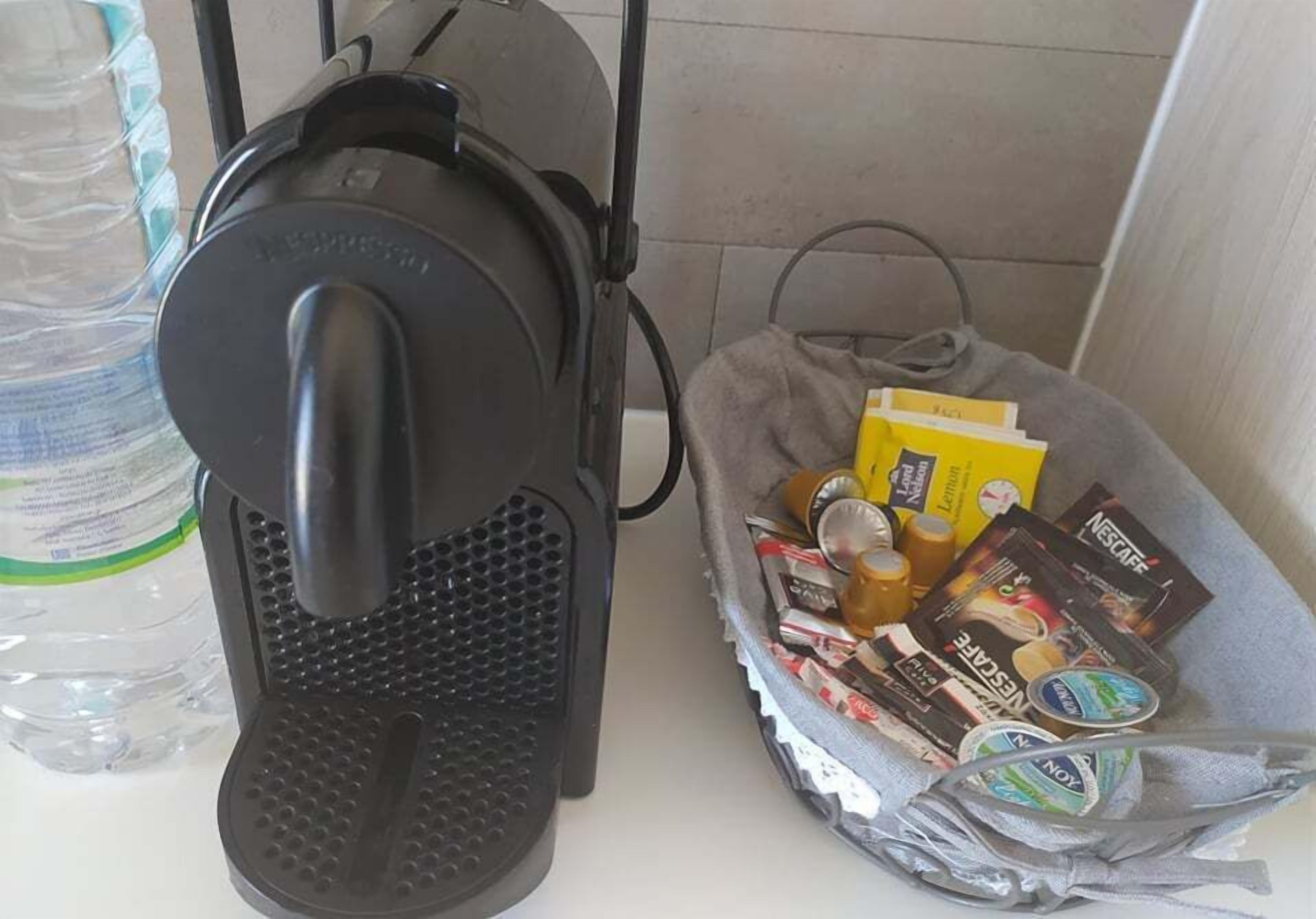Una cafetera, un cesto de cápsulas de café y una botella de agua sobre una encimera.