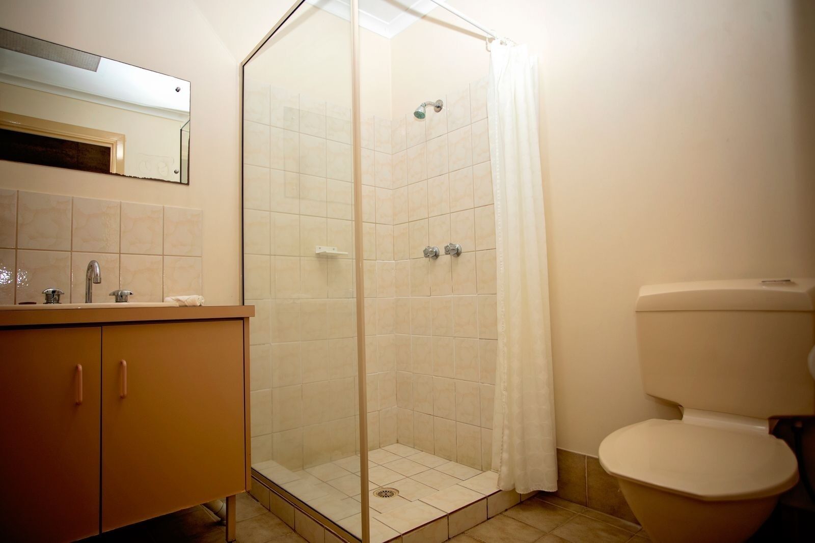 Un baño con ducha de vidrio, inodoro y lavamanos con espejo.