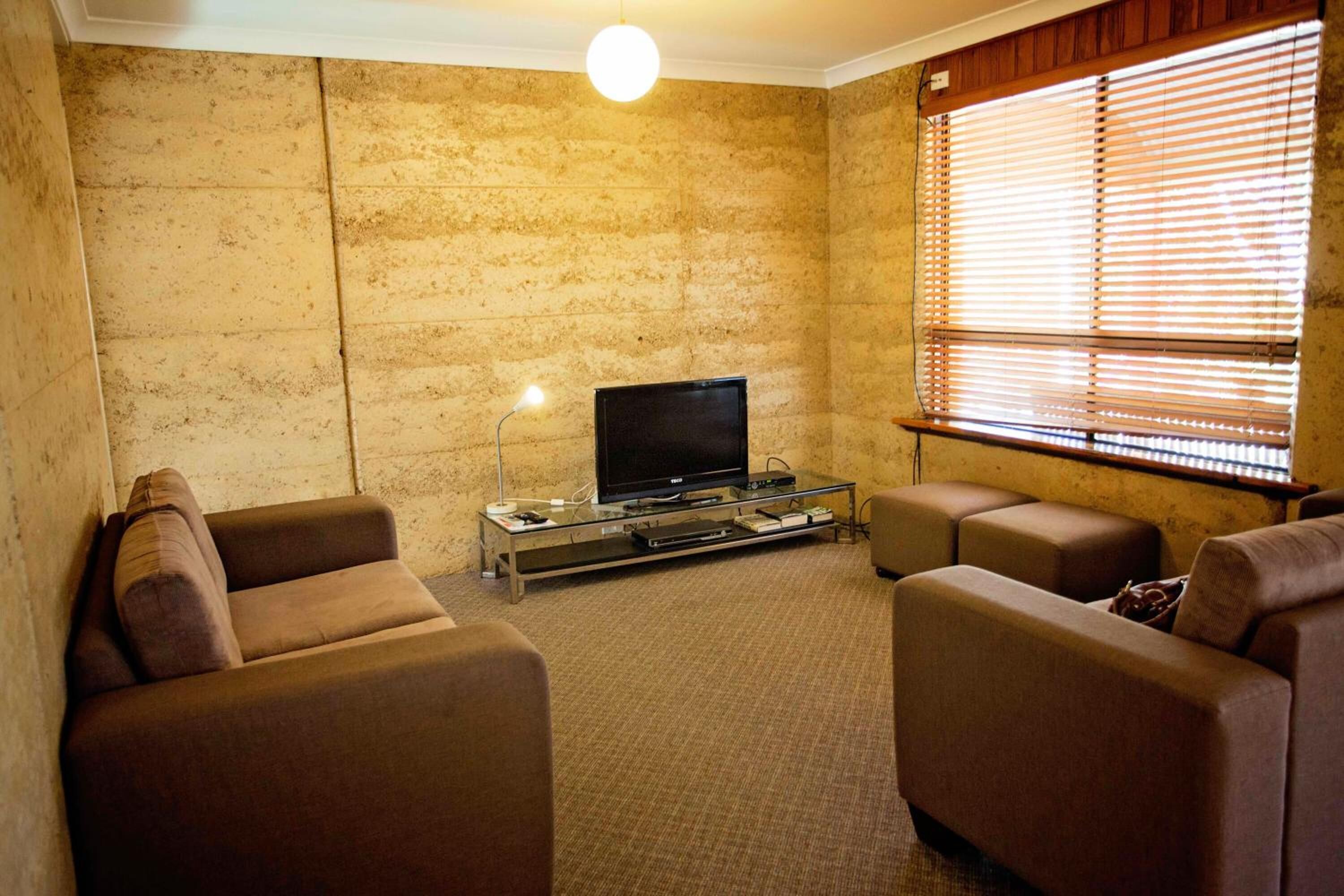 A living room with a flat-screen TV on a glass coffee table, two brown sofas, and a large window with blinds.