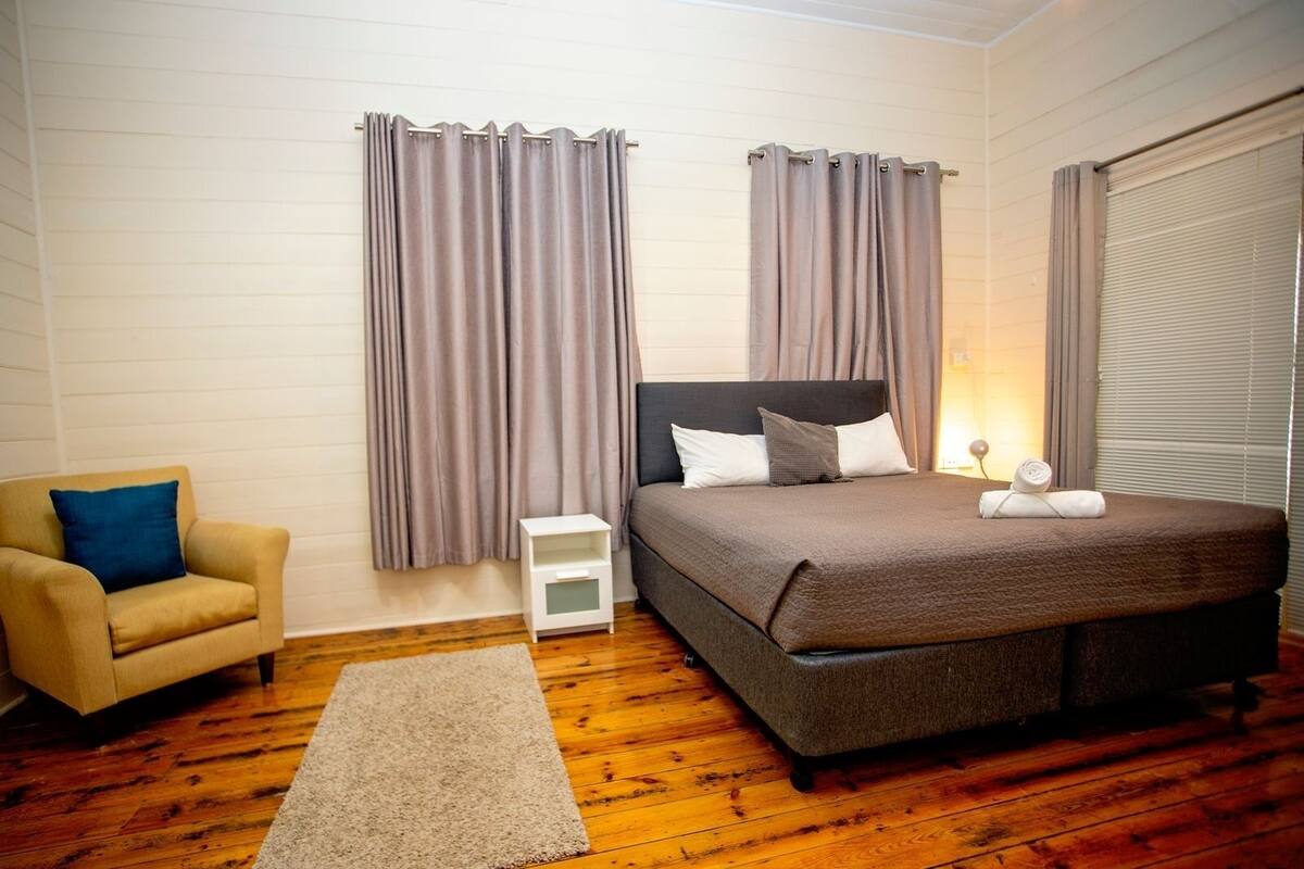 Une chambre à coucher avec un lit, une chaise, une table de chevet et des rideaux.