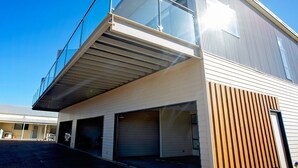 Un bâtiment moderne doté d’un balcon en verre, de plusieurs portes de garage et d’un toit en pente.